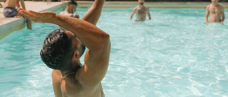 A swimming pool with people playing volleyball.