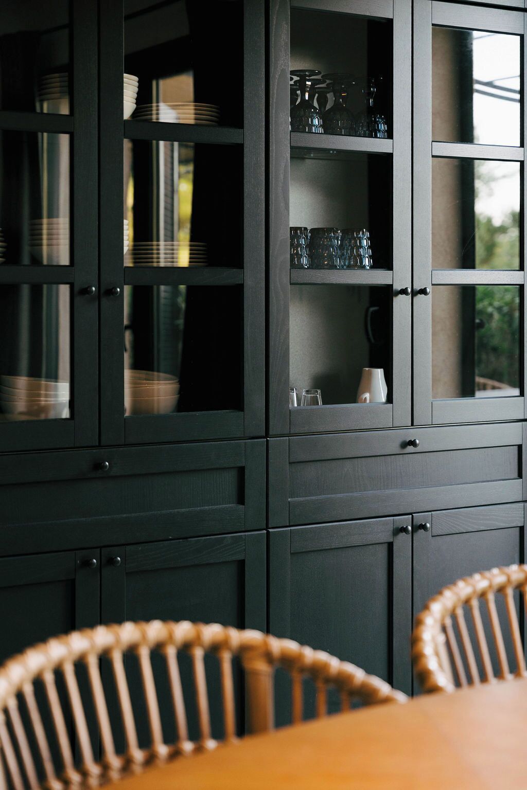 Un mueble de madera oscura con puertas de cristal, que contiene platos, vasos y una jarra.