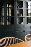 Un mueble de madera oscura con puertas de cristal, que contiene platos, vasos y una jarra.
