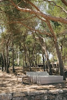 Un área de estar al aire libre y apartada, con un muro de piedra y un banco, rodeada de altos árboles.