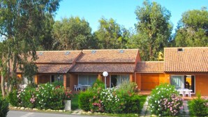 A two-story building with a tiled roof, a front porch with a table and chairs, and a garden with flowering plants. - Résidence Marina Corsa (Ghisonaccia)