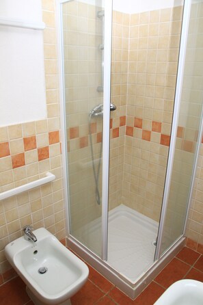 Un baño con ducha de vidrio, lavamanos blanco y paredes de azulejos.