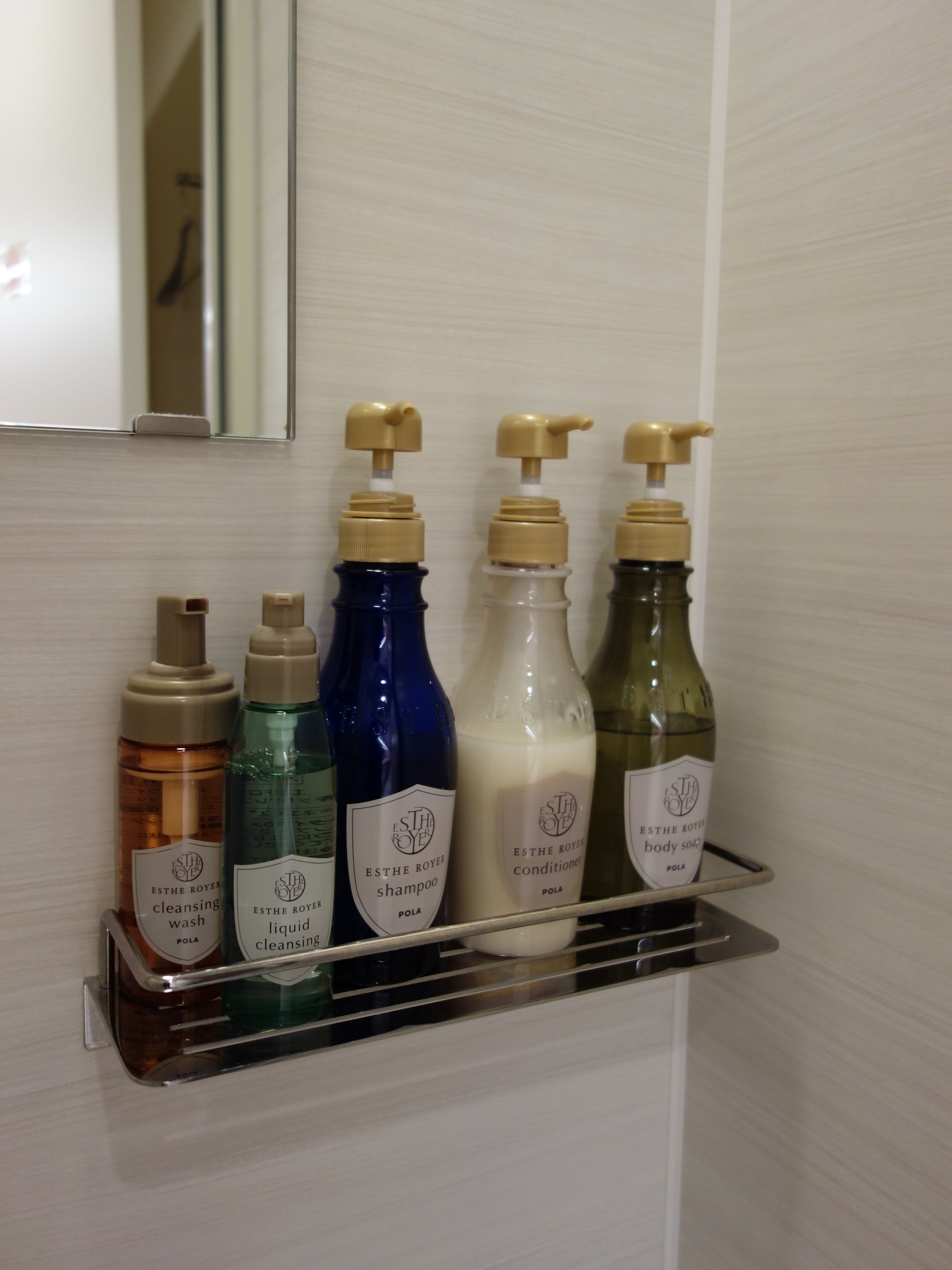 A bathroom shelf with various toiletries including a cleansing wash, liquid cleansing, shampoo, conditioner, and body wash.