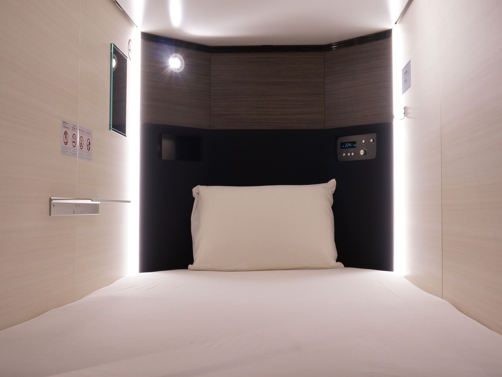 A hotel room with a bed, a control panel, and a wall-mounted light.