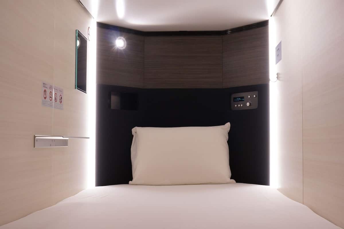 Una habitación de hotel con una cama, un panel de control y una lámpara fijada a la pared.