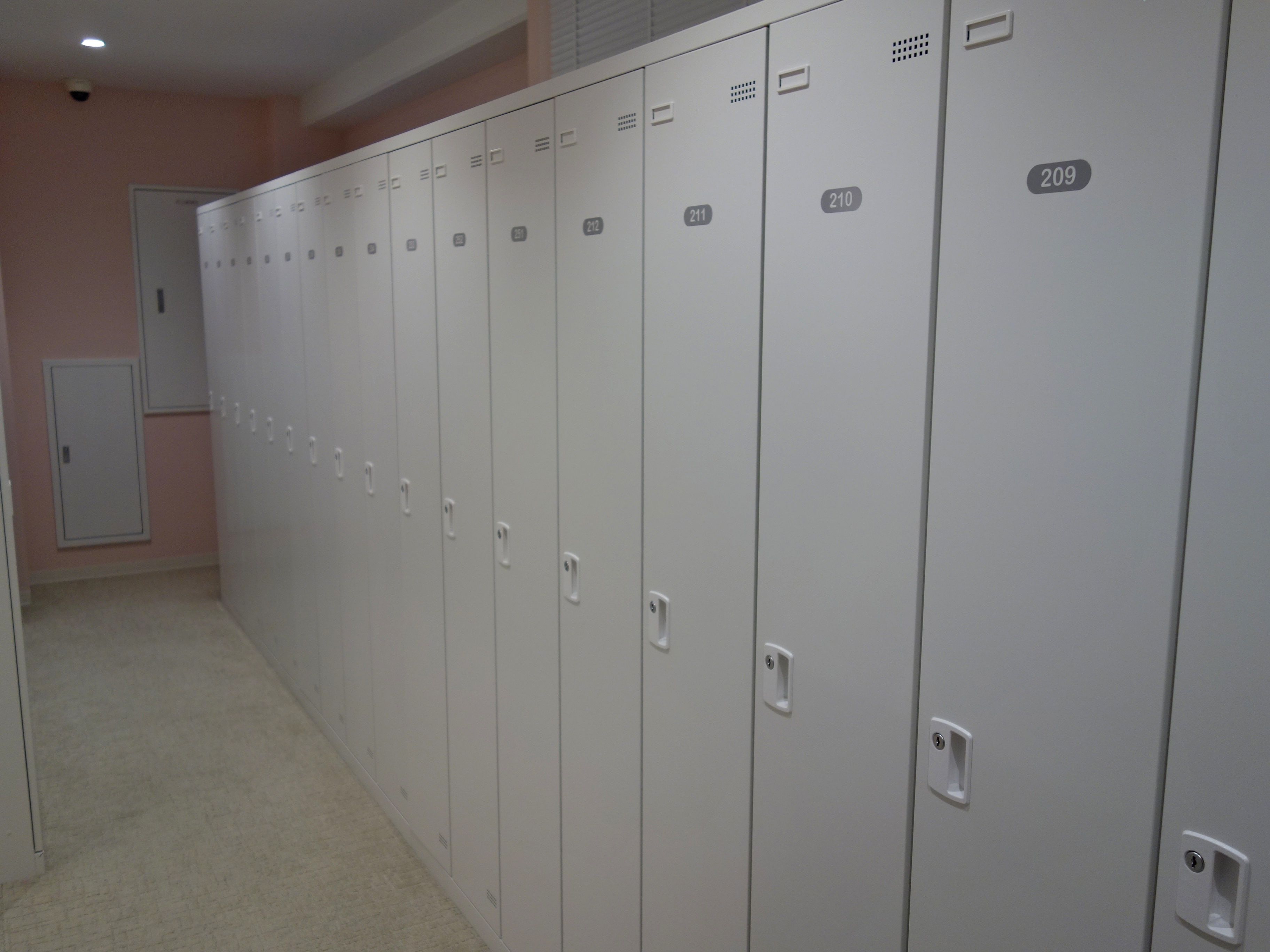 A row of white lockers numbered 209 to 212 in a hallway with a beige carpet.