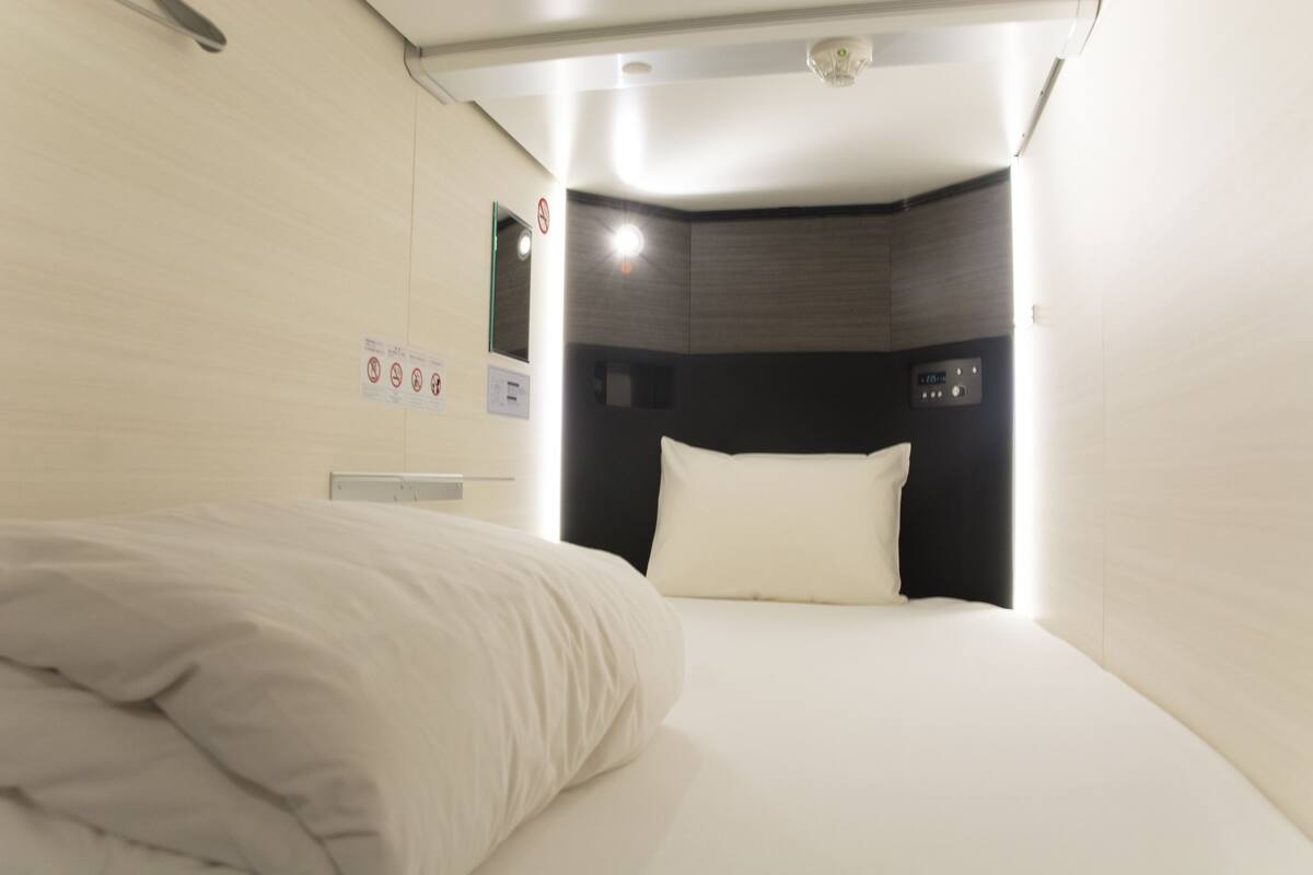 Una habitación de hotel con una cama bien hecha, un cabecero con panel de control y una lámpara de pared.