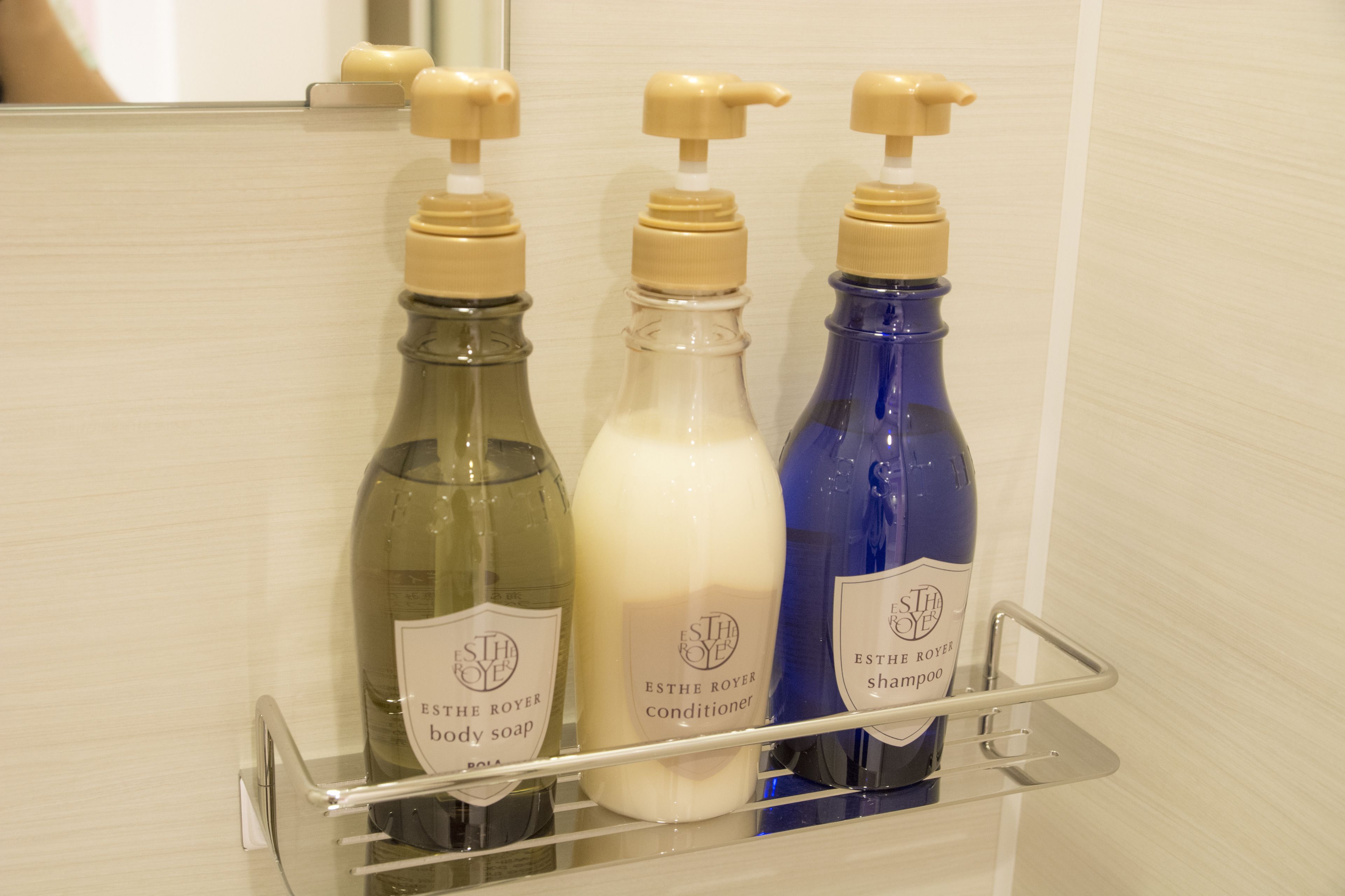 A bathroom shelf with three bottles of ESTHE ROYER body soap, conditioner, and shampoo.