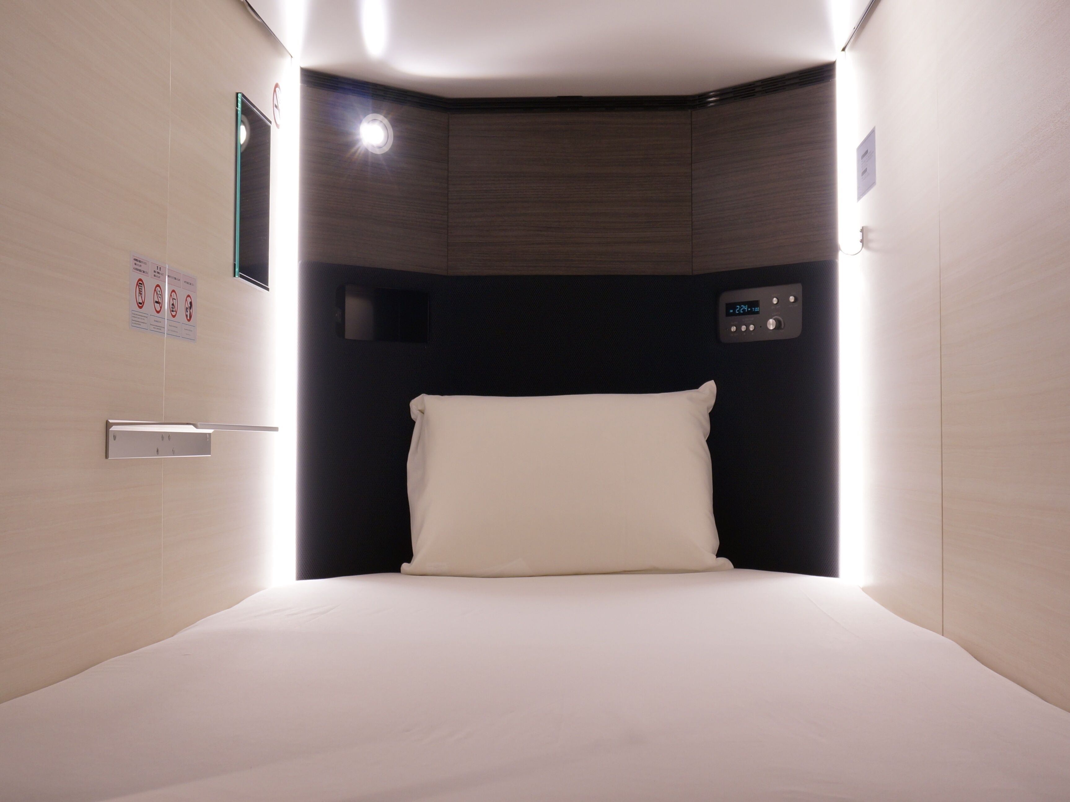 A hotel room with a bed, a control panel, and a wall-mounted light.