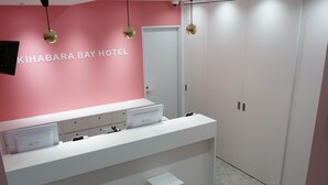 Zona de recepción de un hotel con pared rosa, mostrador de recepción y una puerta.