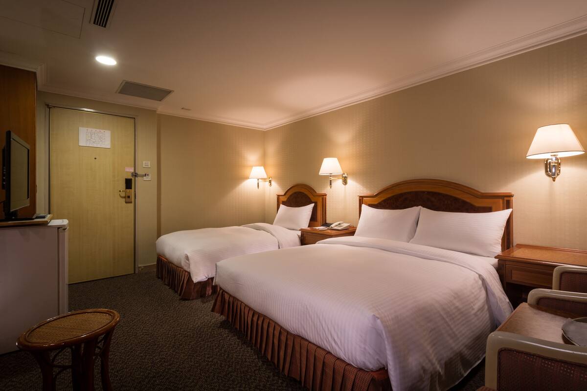 A hotel room with two beds, a desk, a chair, and a door with a sign.