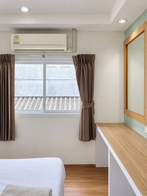 A hotel room with a bed, a window with curtains, an air conditioning unit, and a wooden counter. - Sleep at Phuket (Phuket)