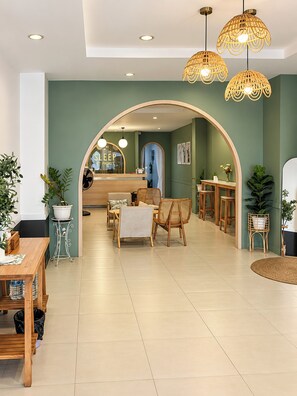 Un hall d’hôtel spacieux avec un espace salon central, un comptoir d’accueil et une grande porte en arc donnant sur la salle à manger.