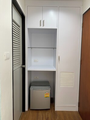 A room with a wardrobe, a small storage unit, and a door with a louvered window. - Sleep at Phuket (Phuket)