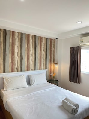 Una camera d'albergo con un letto grande, un pannello di legno a parete, un comodino con una lampada e una finestra con tende.