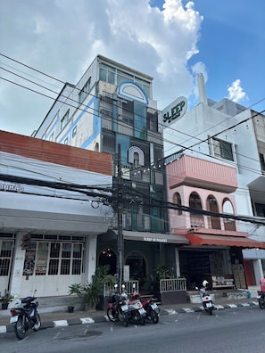Un edificio con un cartello che recita 'SLEEP AT PHUKET' e una motocicletta parcheggiata di fronte.