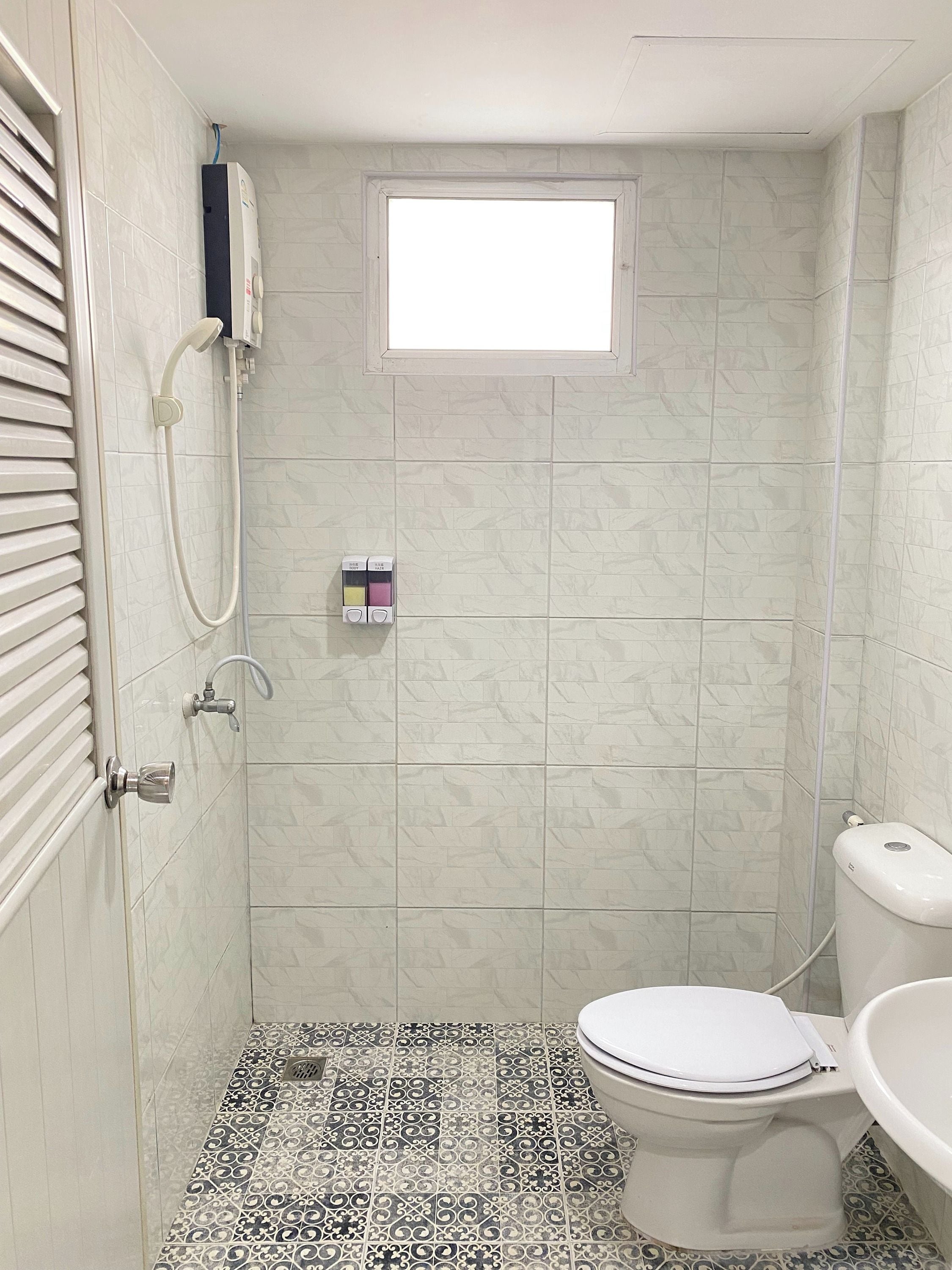 A bathroom with a shower, toilet, and a window.