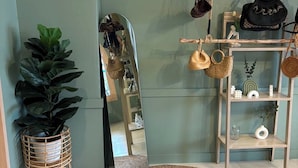 A room with a large mirror, a round woven rug, a potted plant, and a wooden shelf with handbags. - Sleep at Phuket (Phuket)