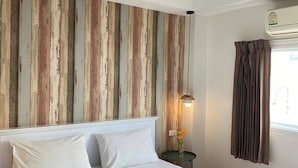 A neatly made bed with white linens, a wooden wall panel, a bedside table with a lamp, and a window with curtains. - Sleep at Phuket (Phuket)