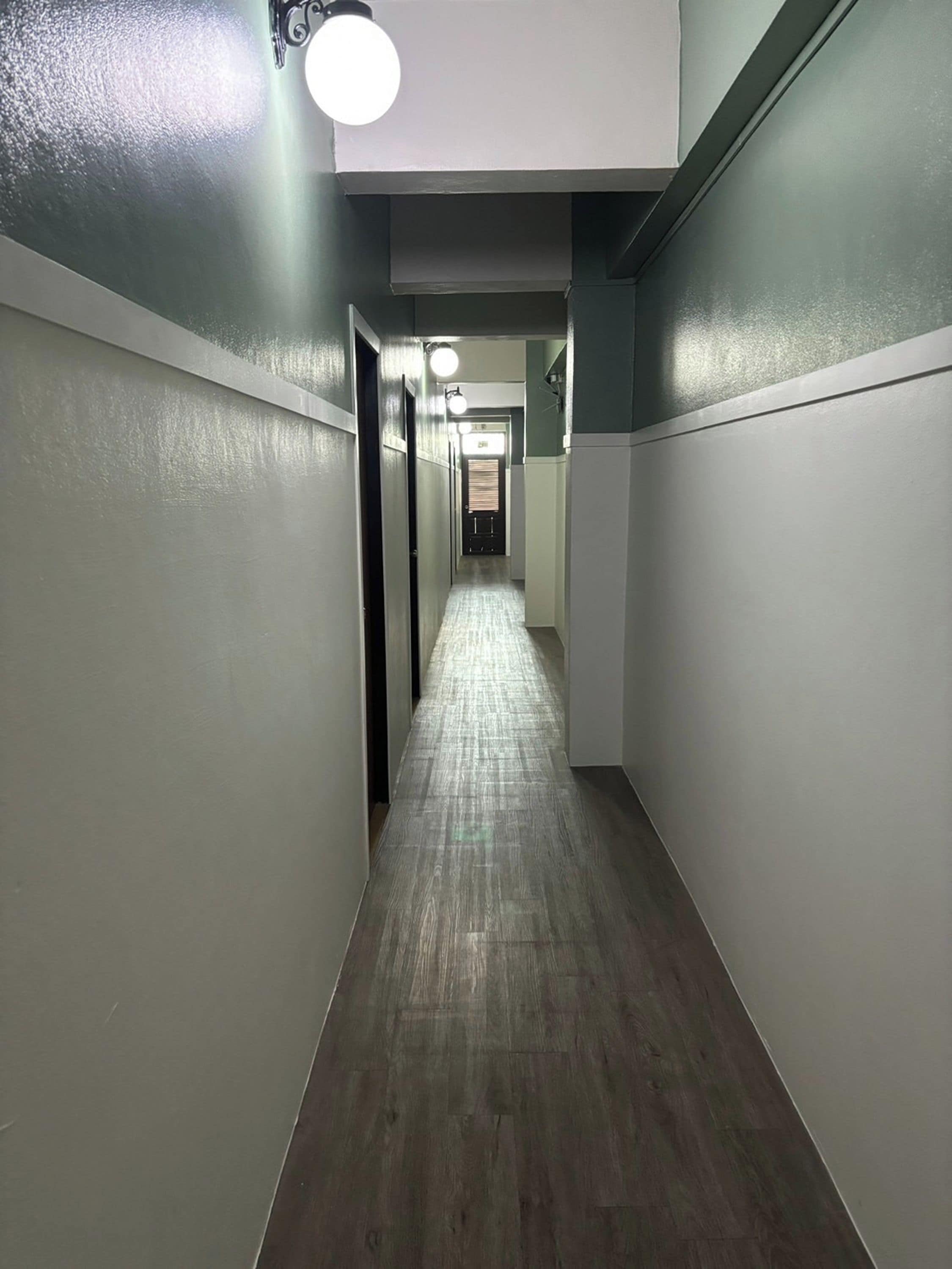 A narrow hallway with a wooden floor and white walls, leading to a door at the end.