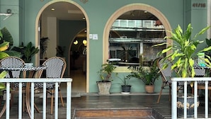 A hotel entrance with a sign reading "SLEEP AT PHUKET". There are outdoor seating areas with tables and chairs, and potted plants are visible. - Sleep at Phuket (Phuket)