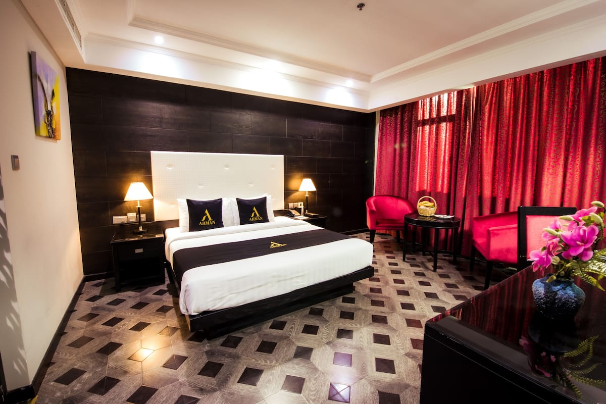 Camera d'albergo con un letto grande, due comodini con lampade, una poltrona rossa, un tavolino con un vaso di fiori e una testiera in legno scuro.
