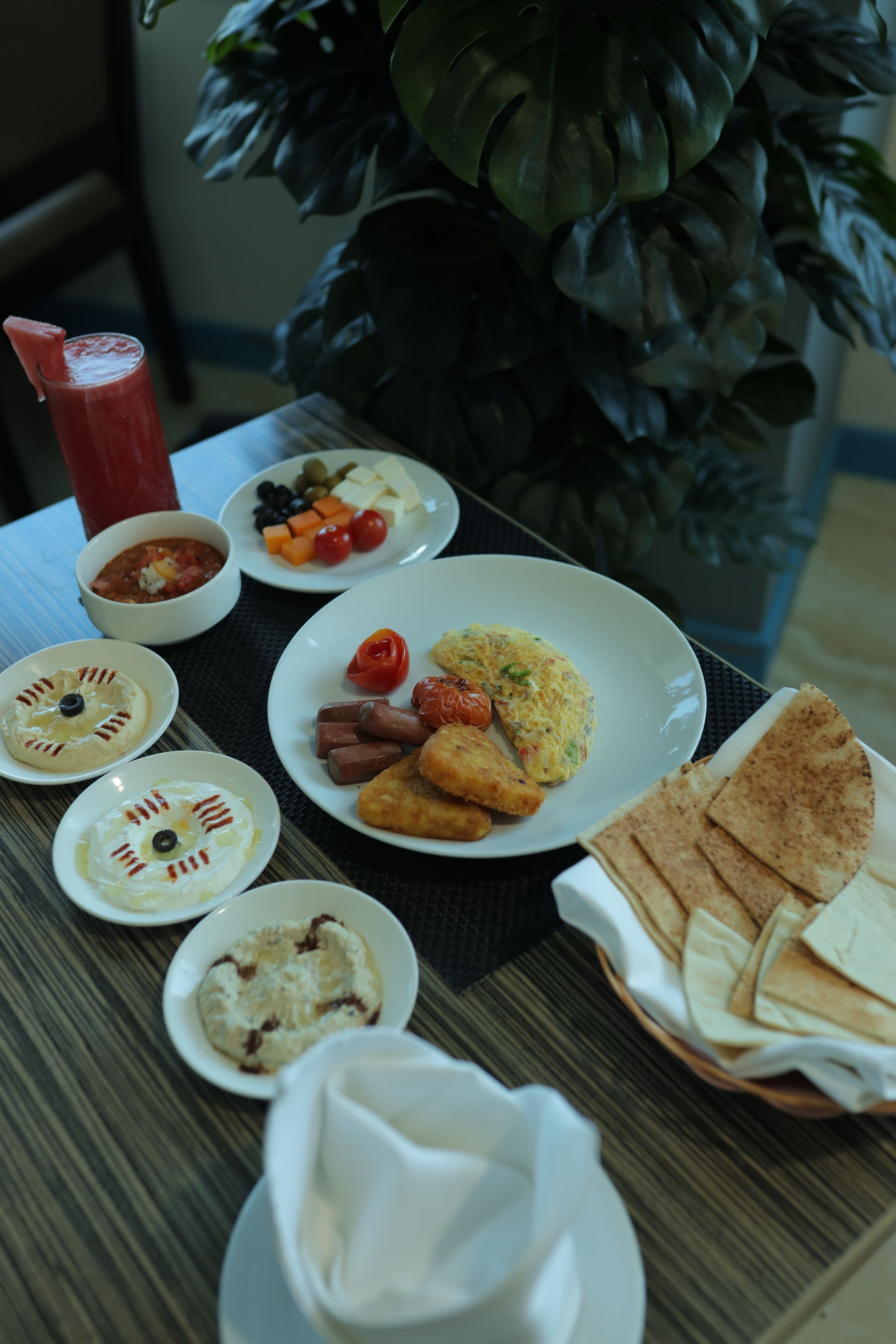 Une table garnie de divers plats, notamment une assiette avec des œufs, des tomates et du fromage, des bols contenant des sauces et un panier de pains plats.