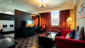Una habitación de hotel con cama, televisión, escritorio, sofá rojo y vista a la ciudad.