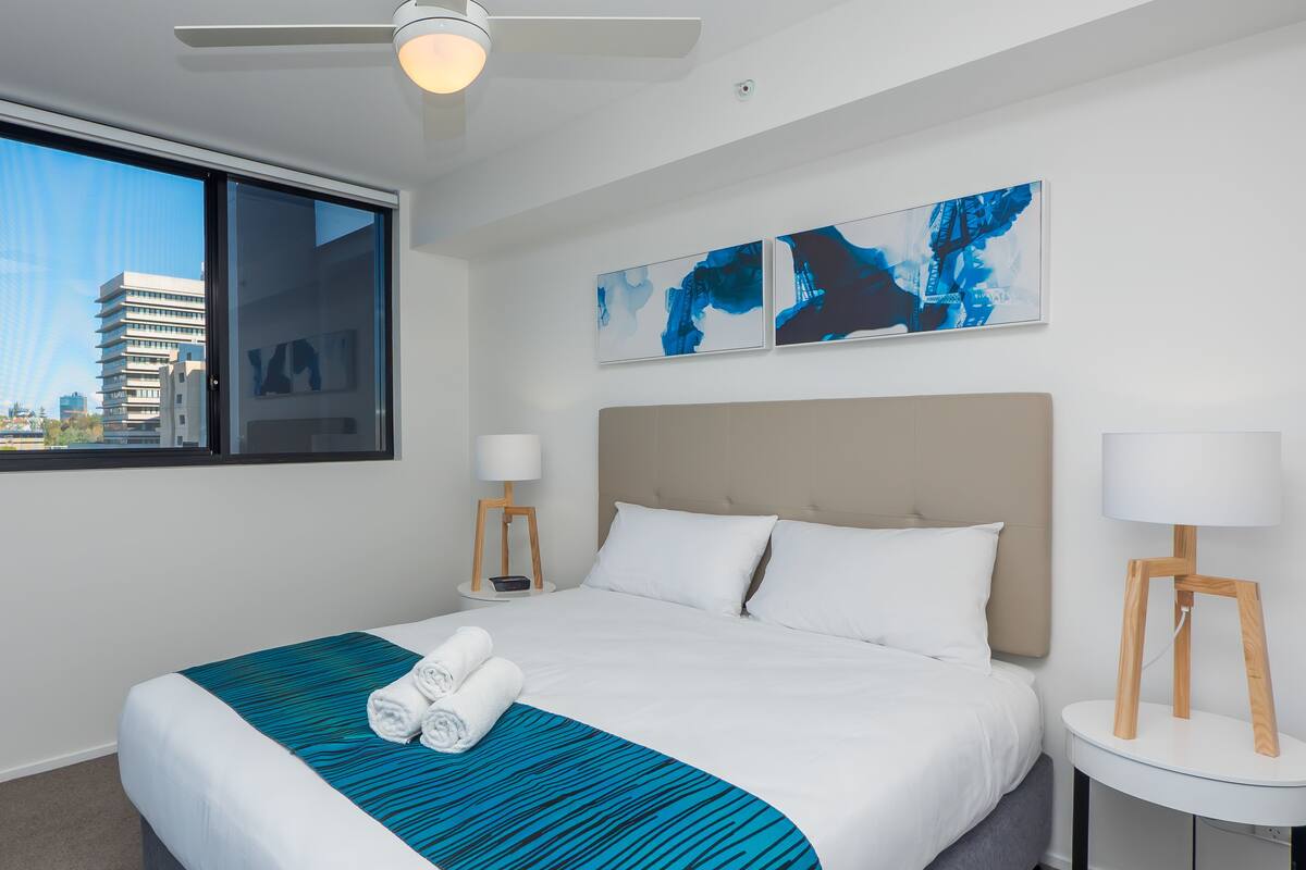 Une chambre d’hôtel avec un grand lit, deux tables de chevet, un ventilateur de plafond et des œuvres d’art accrochées au mur.
