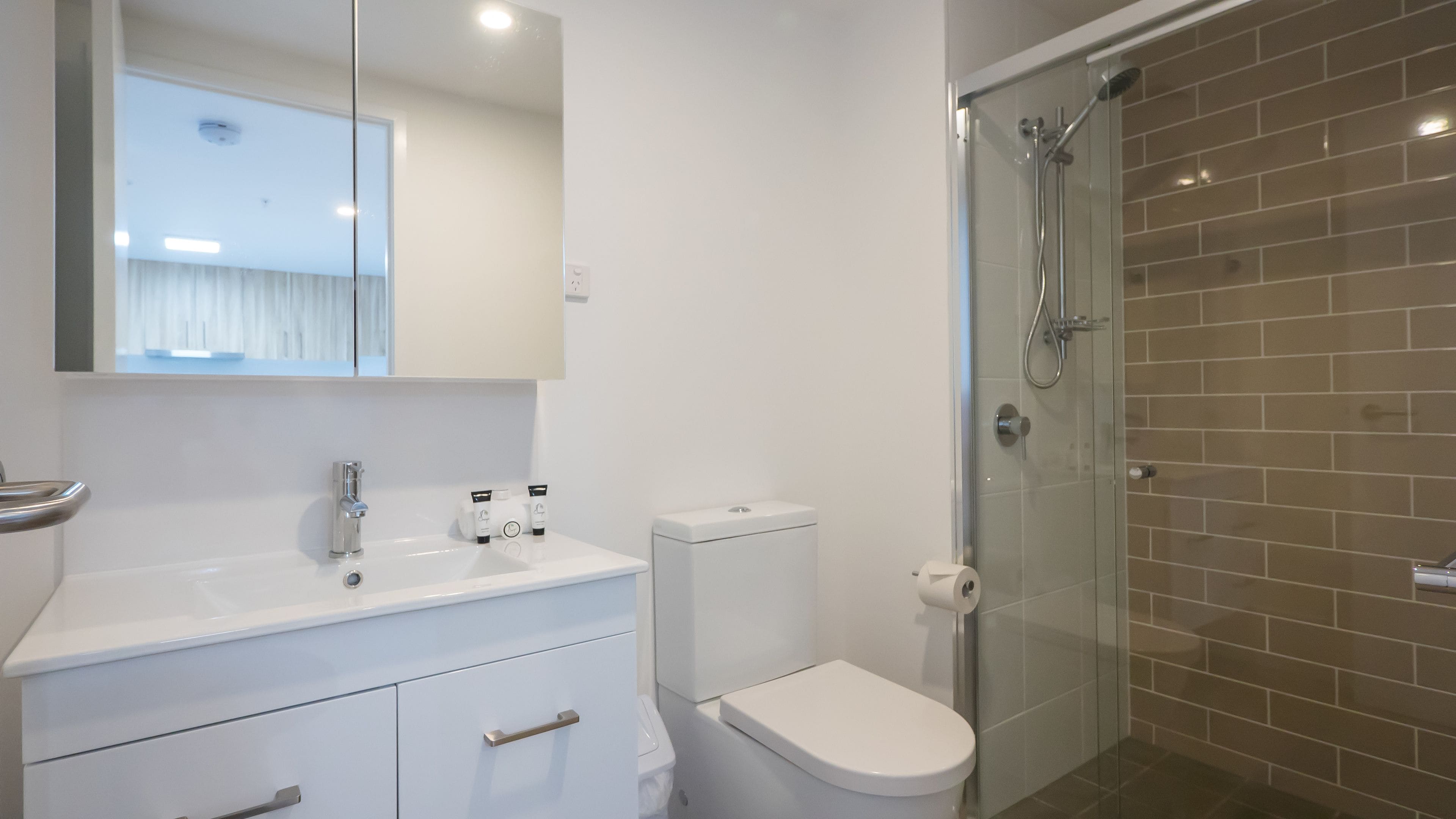 A modern bathroom with a white sink, toilet, and glass shower enclosure.