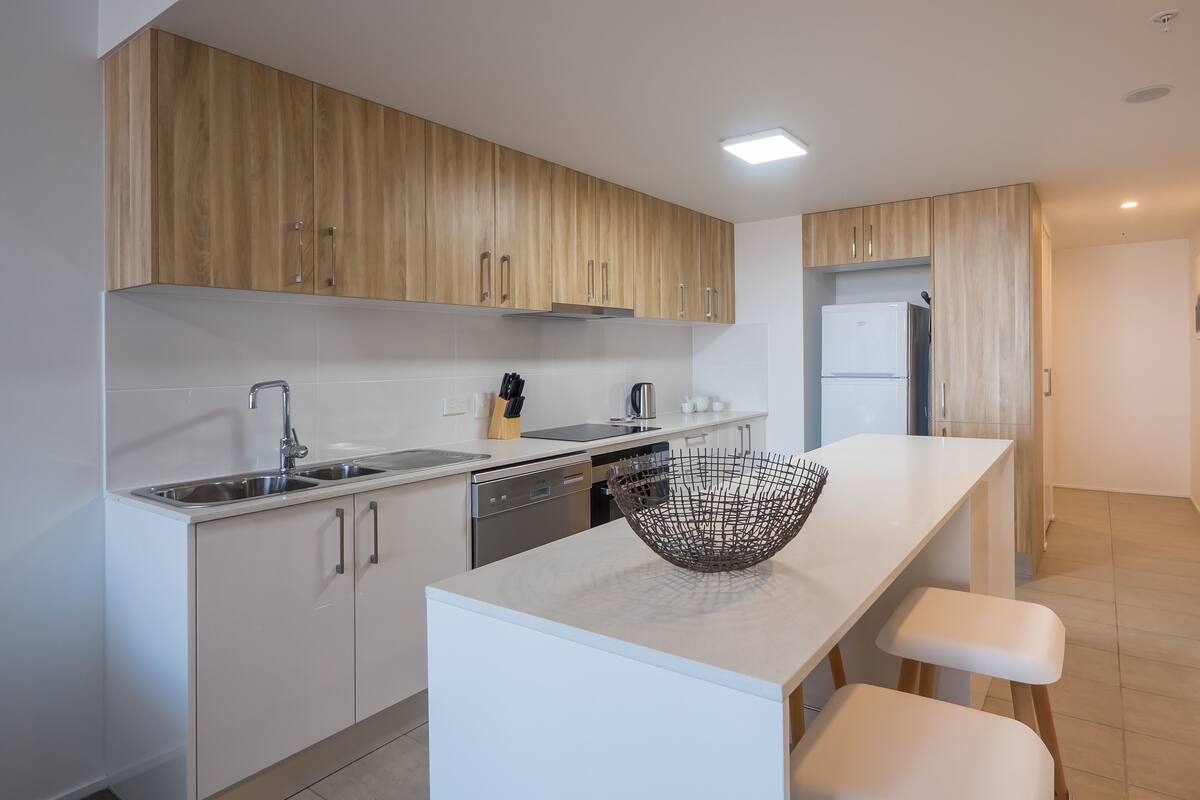 Une cuisine moderne avec des meubles en bois, des appareils en acier inoxydable et un plan de travail blanc.