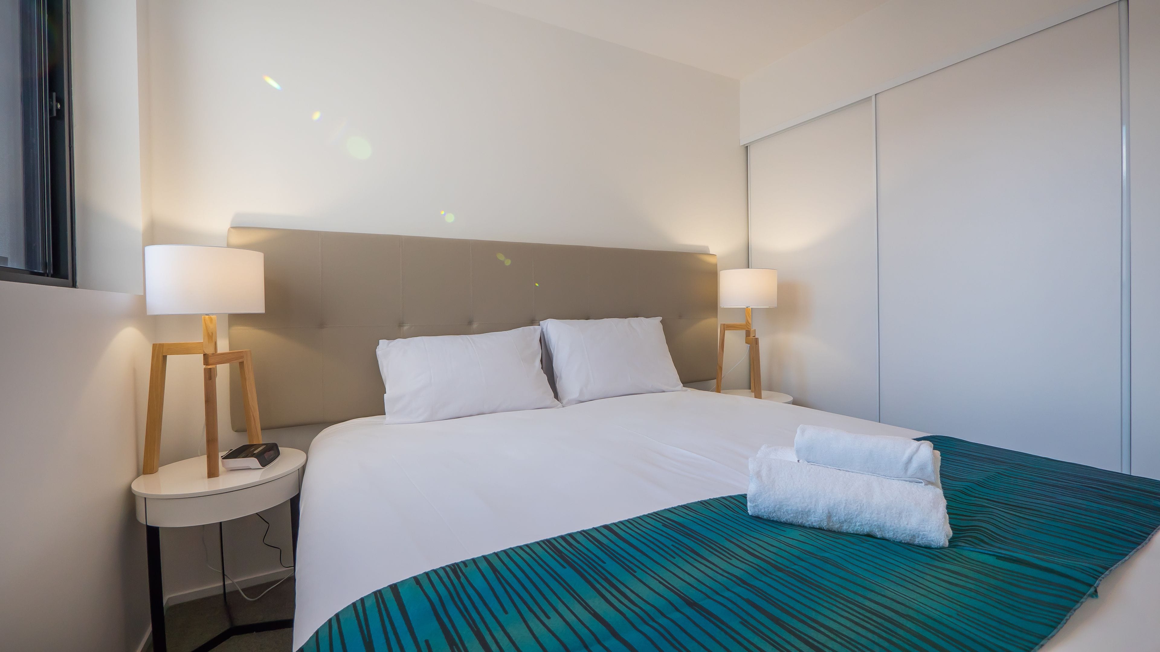 A hotel room with a large bed, two bedside tables with lamps, a headboard, and a blue-striped bedspread.