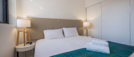 A hotel room with a large bed, two bedside tables with lamps, a headboard, and a blue-striped bedspread.