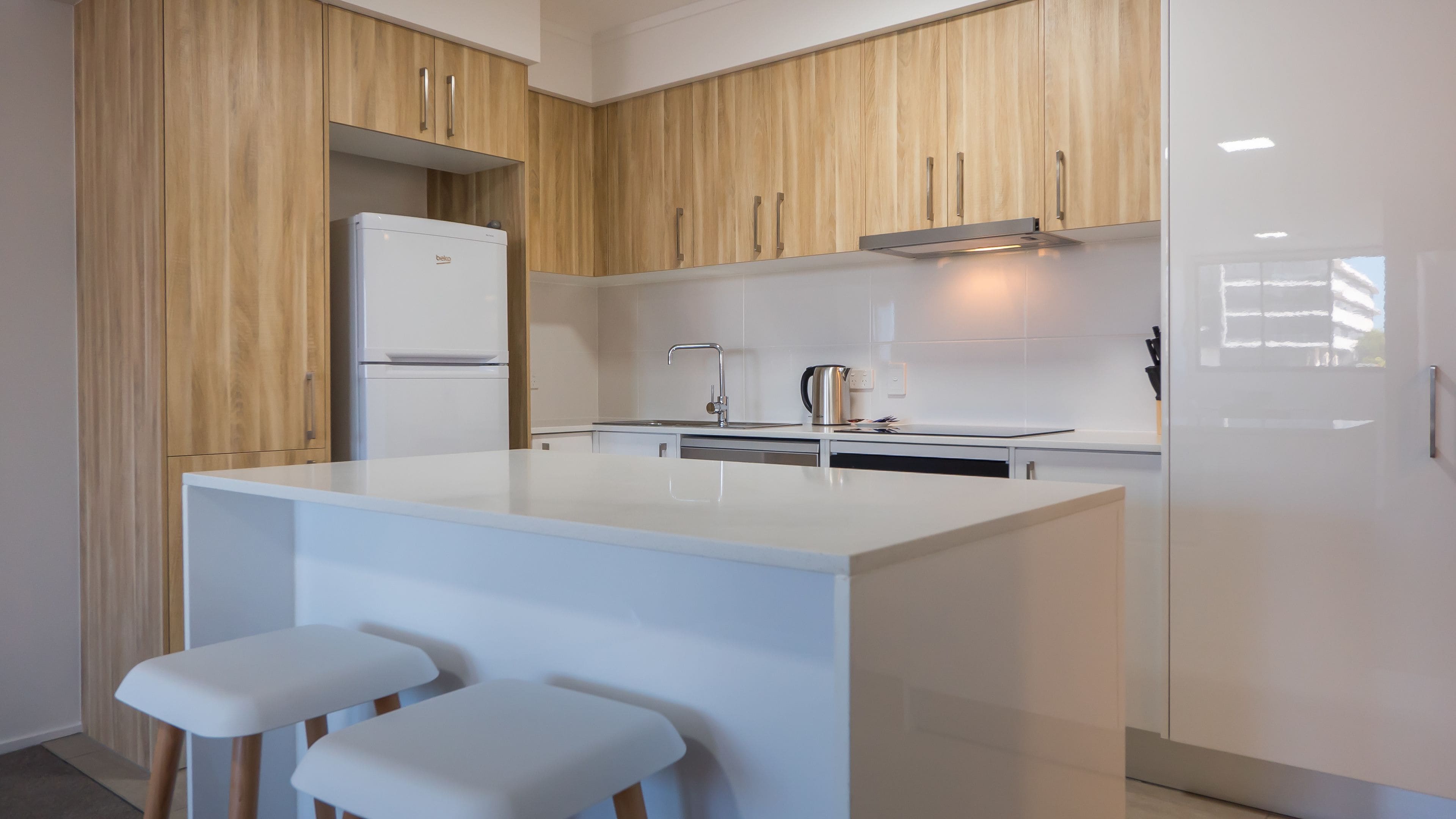 Una cocina moderna con armarios de madera, un refrigerador blanco, un lavamanos y una pequeña isla con taburetes.