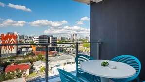 Un balcón con mesa y sillas, con vista a un paisaje urbano de edificios modernos y cielo despejado.
