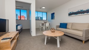 Una sala de estar moderna con un sofá, una mesa de centro y un televisor. Hay un comedor con una mesa y sillas.