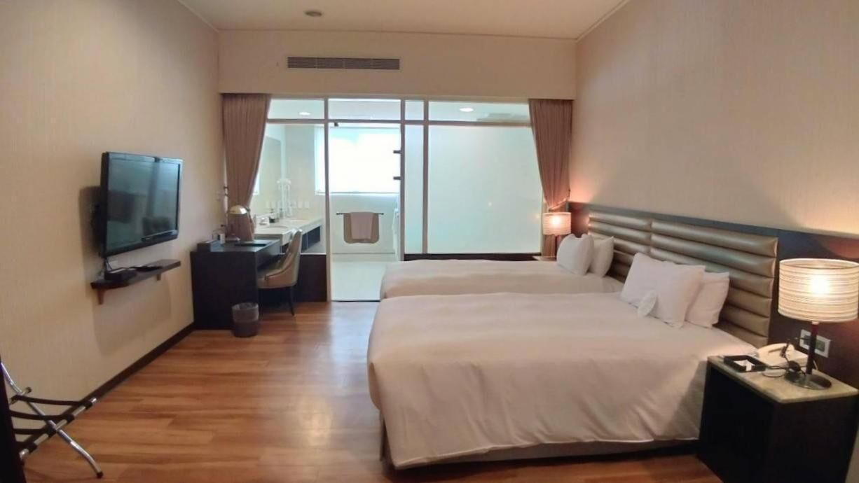 A hotel room with a large bed, a TV, a desk, and a sliding door to a balcony.