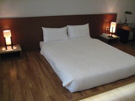 Una cama bien hecha con sábanas blancas, dos mesitas de noche con lámparas y un cabecero de madera.