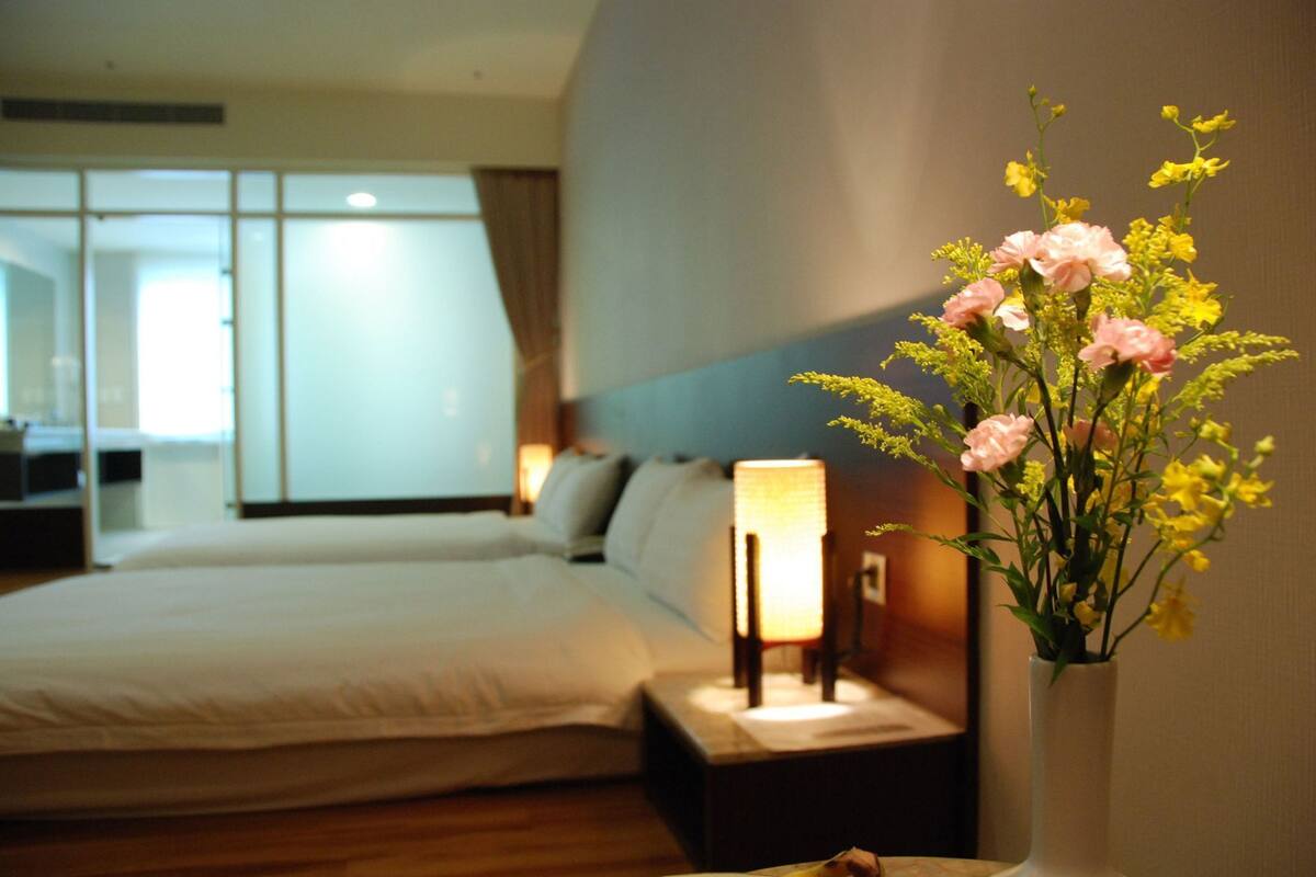 A hotel room with a bed, a nightstand with a lamp, and a vase of flowers.