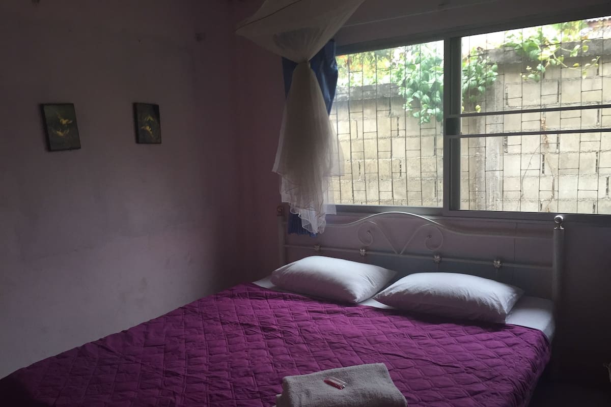 Una cama individual con un edredón morado, una almohada blanca y una toalla doblada.