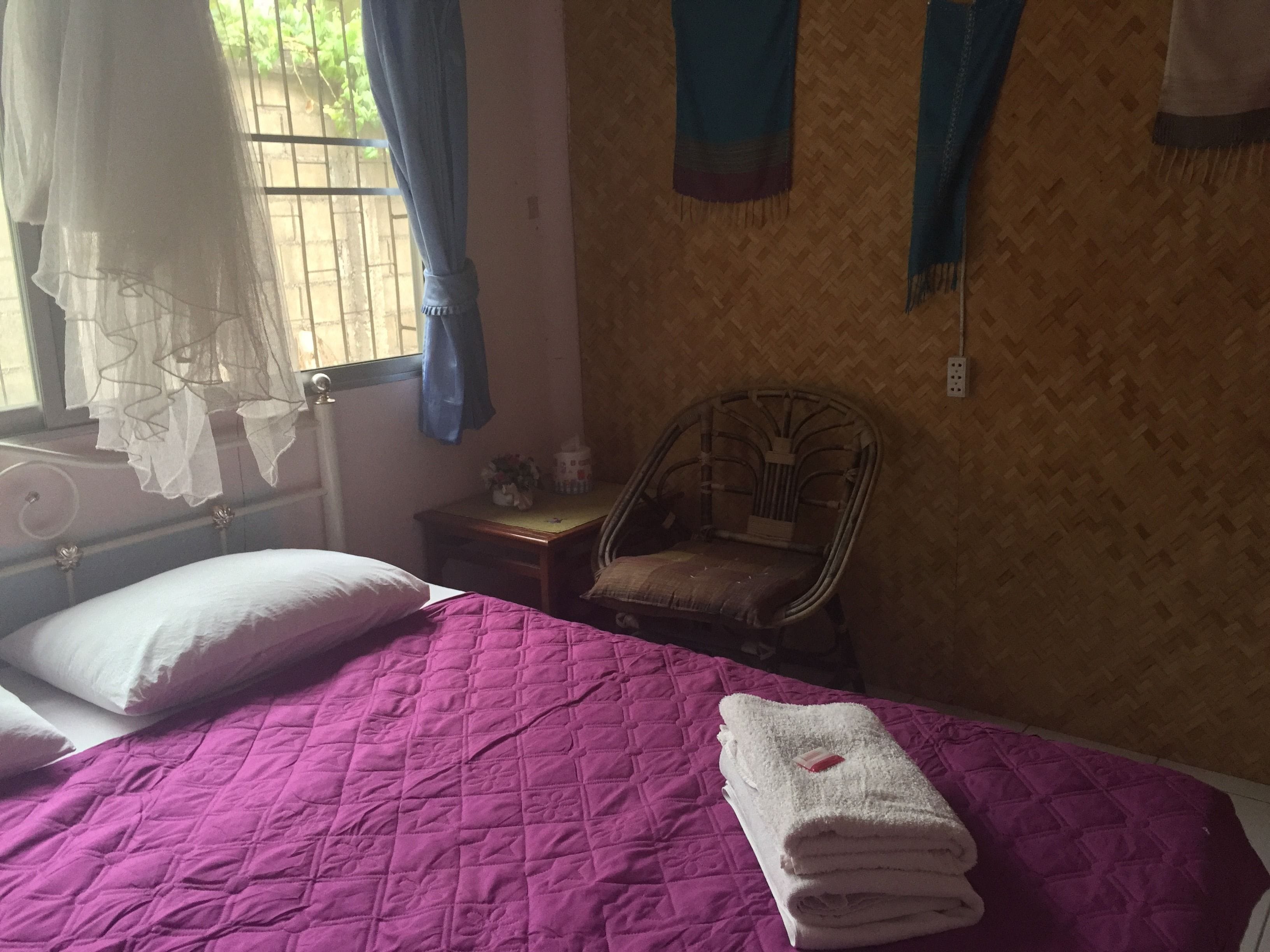 Habitació amb llit, cadira i finestra amb cortines.