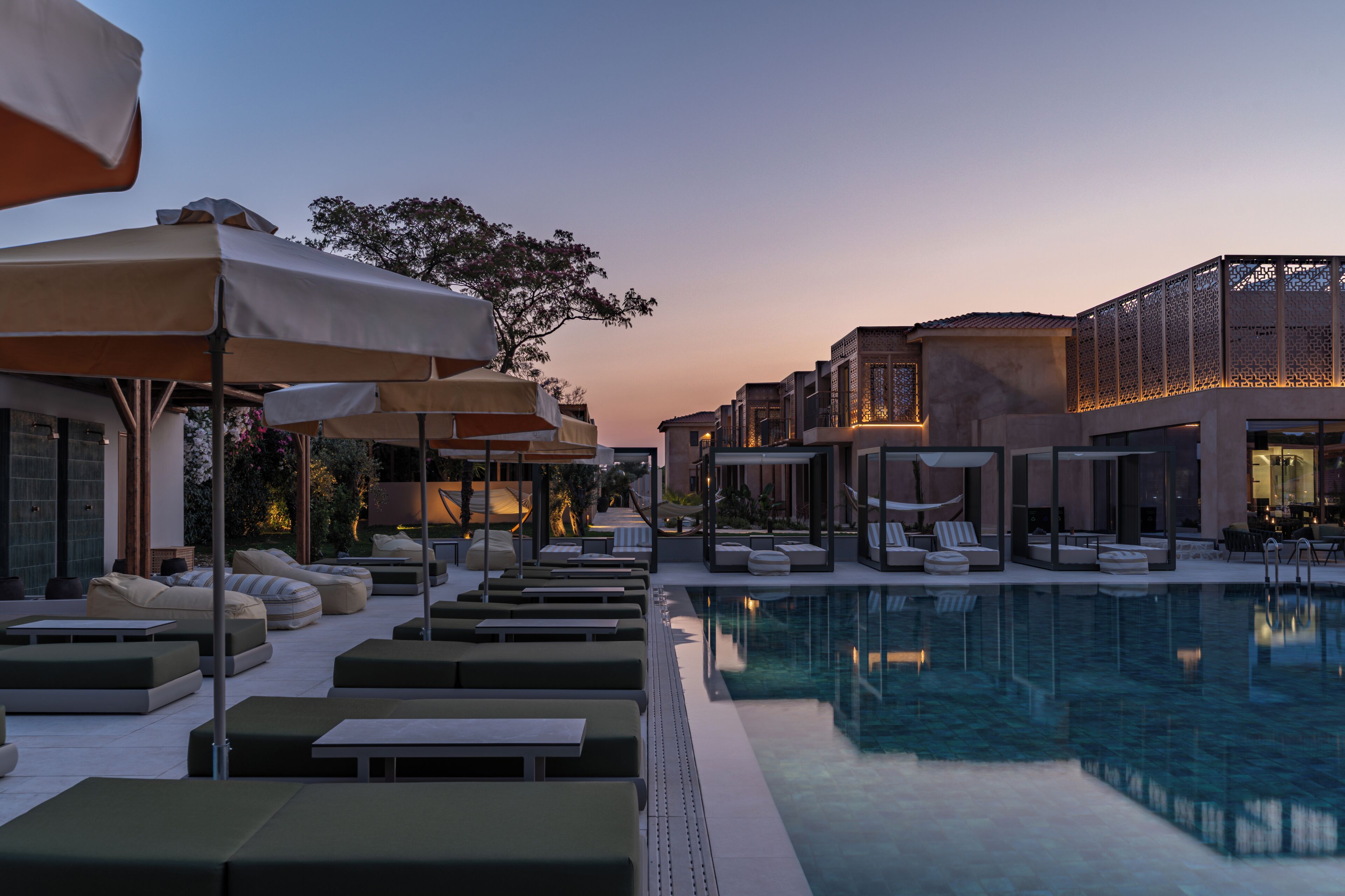 A poolside area with lounge chairs and umbrellas, a clear pool, and modern buildings in the background.