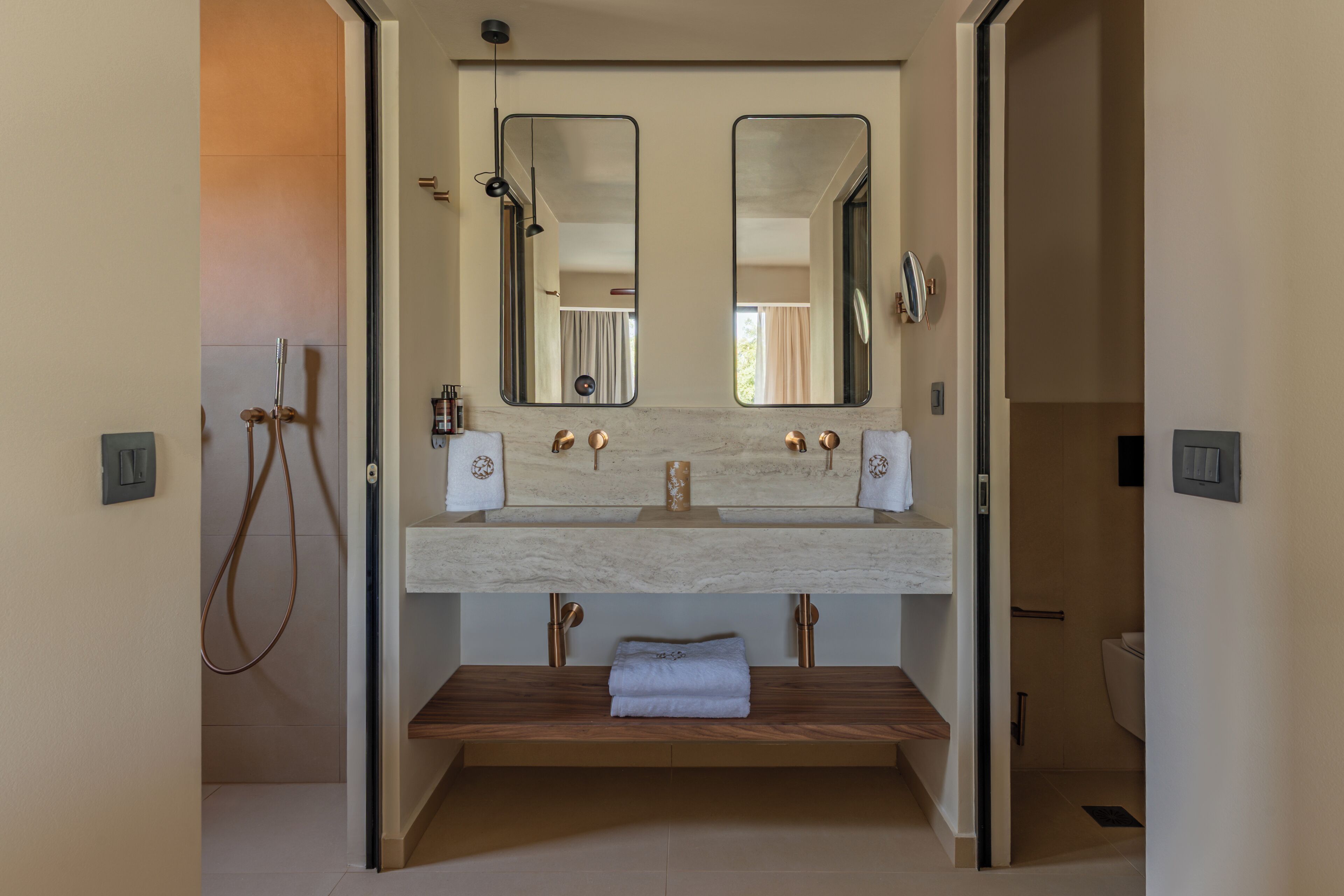 A modern bathroom with a double sink, two mirrors, a towel rack, and a wooden bench.