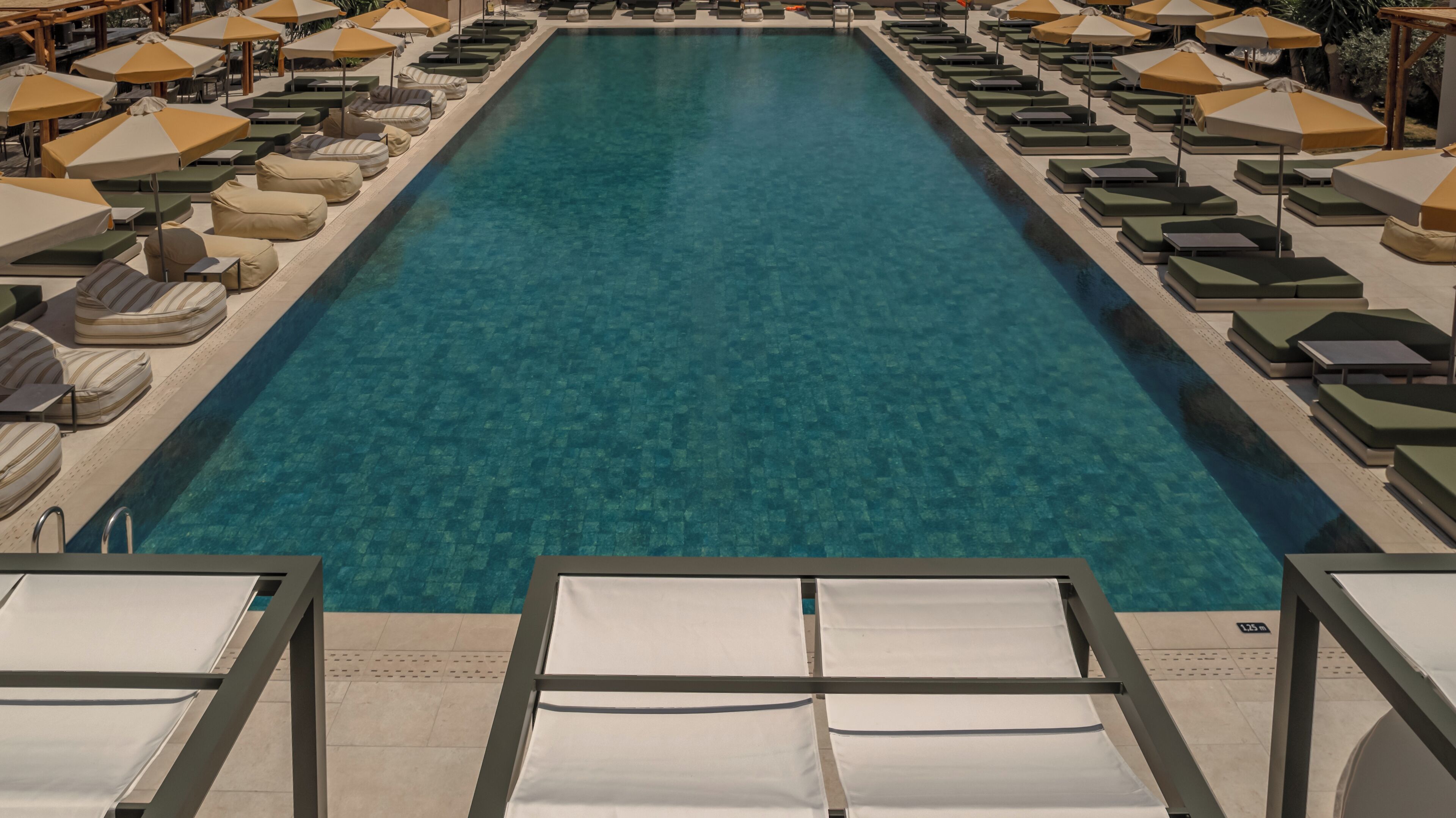 A long, rectangular pool with lounge chairs and umbrellas on both sides.