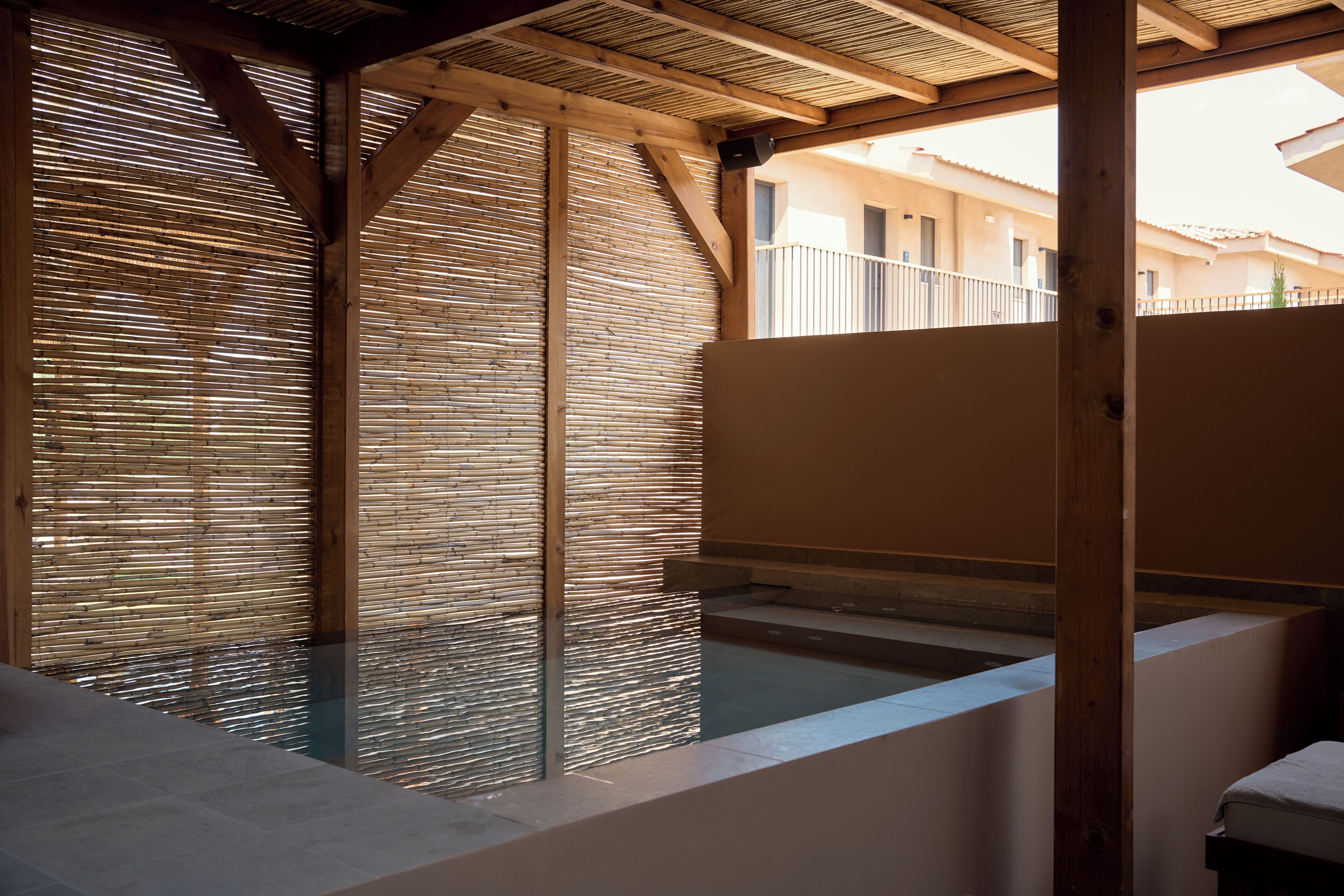Una habitación con separador de bambú, una piscina pequeña y vista a un edificio.