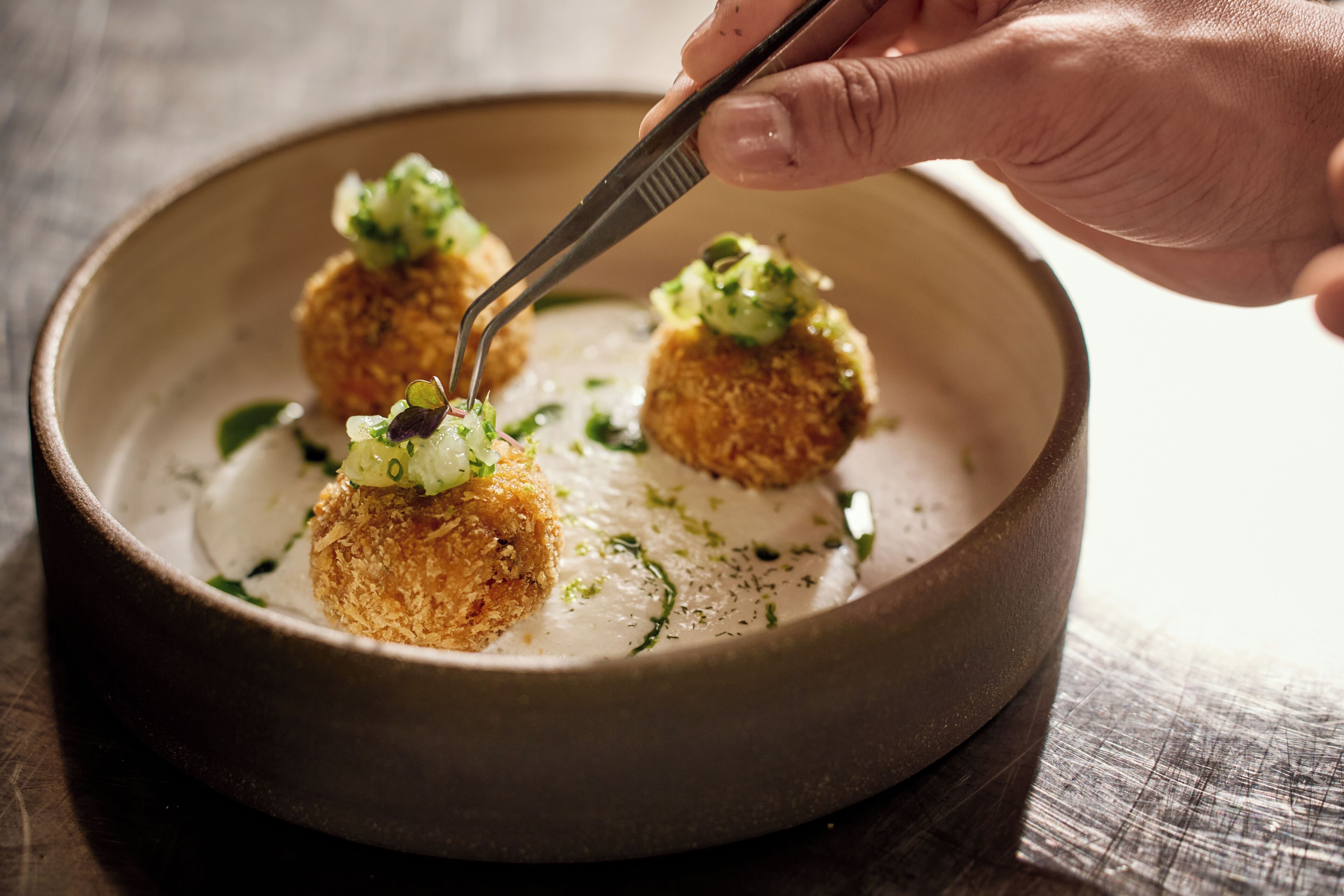 A bowl of food with a hand using tongs to pick up a piece.