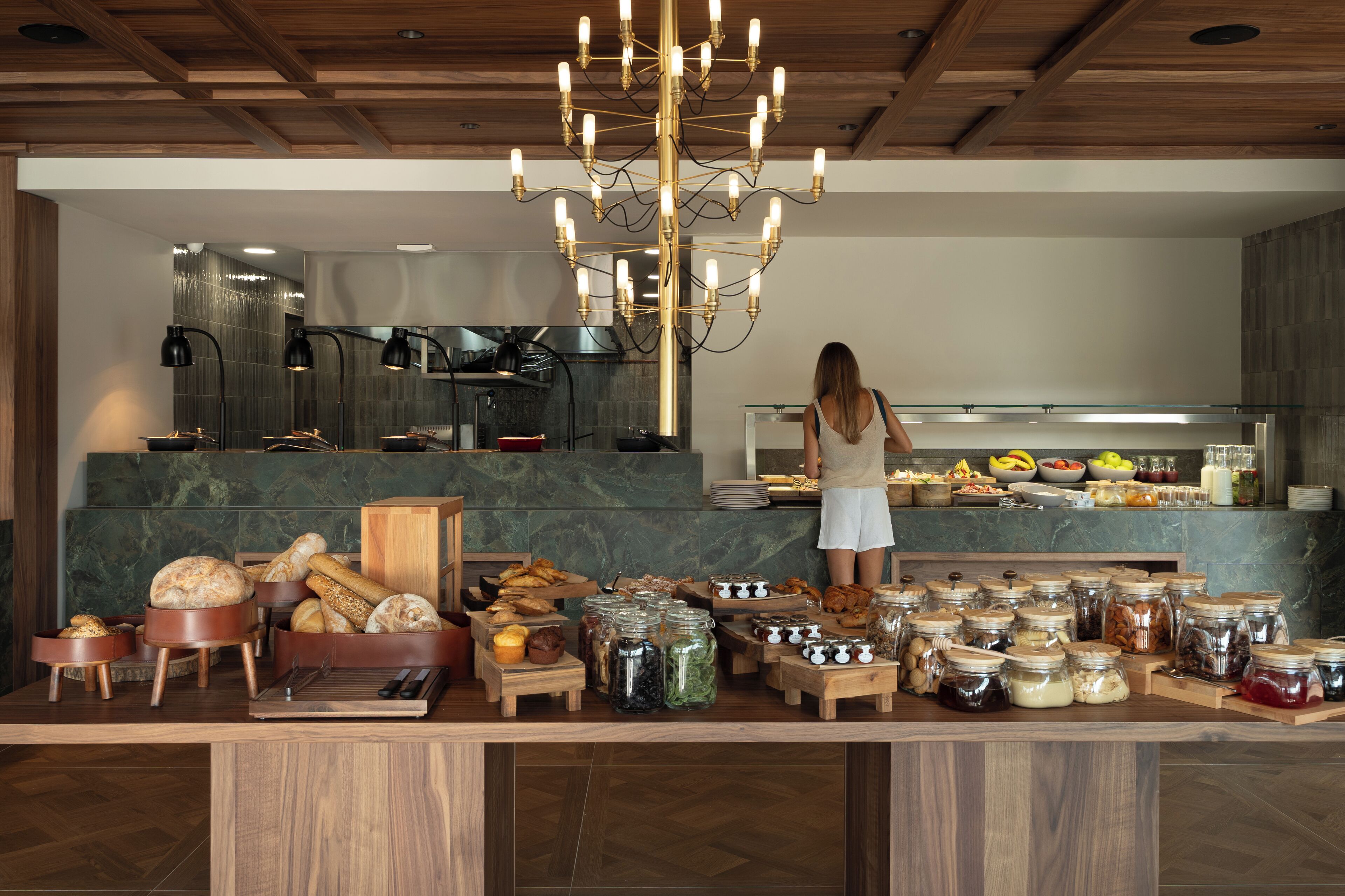 A breakfast buffet with various food items and a woman standing at the counter.