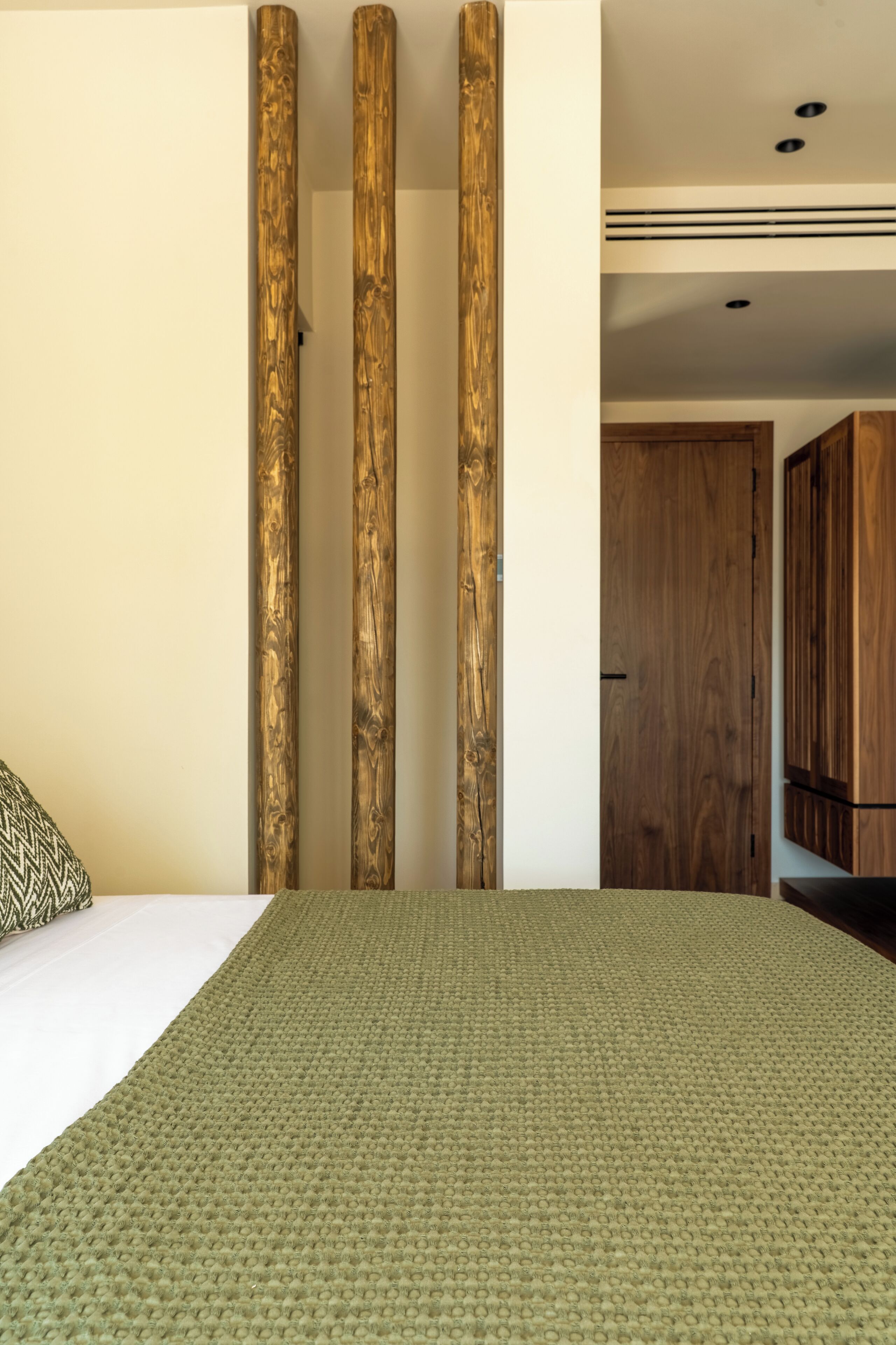 Una camera da letto con un letto, un tappeto verde con trama e pilastri in legno.