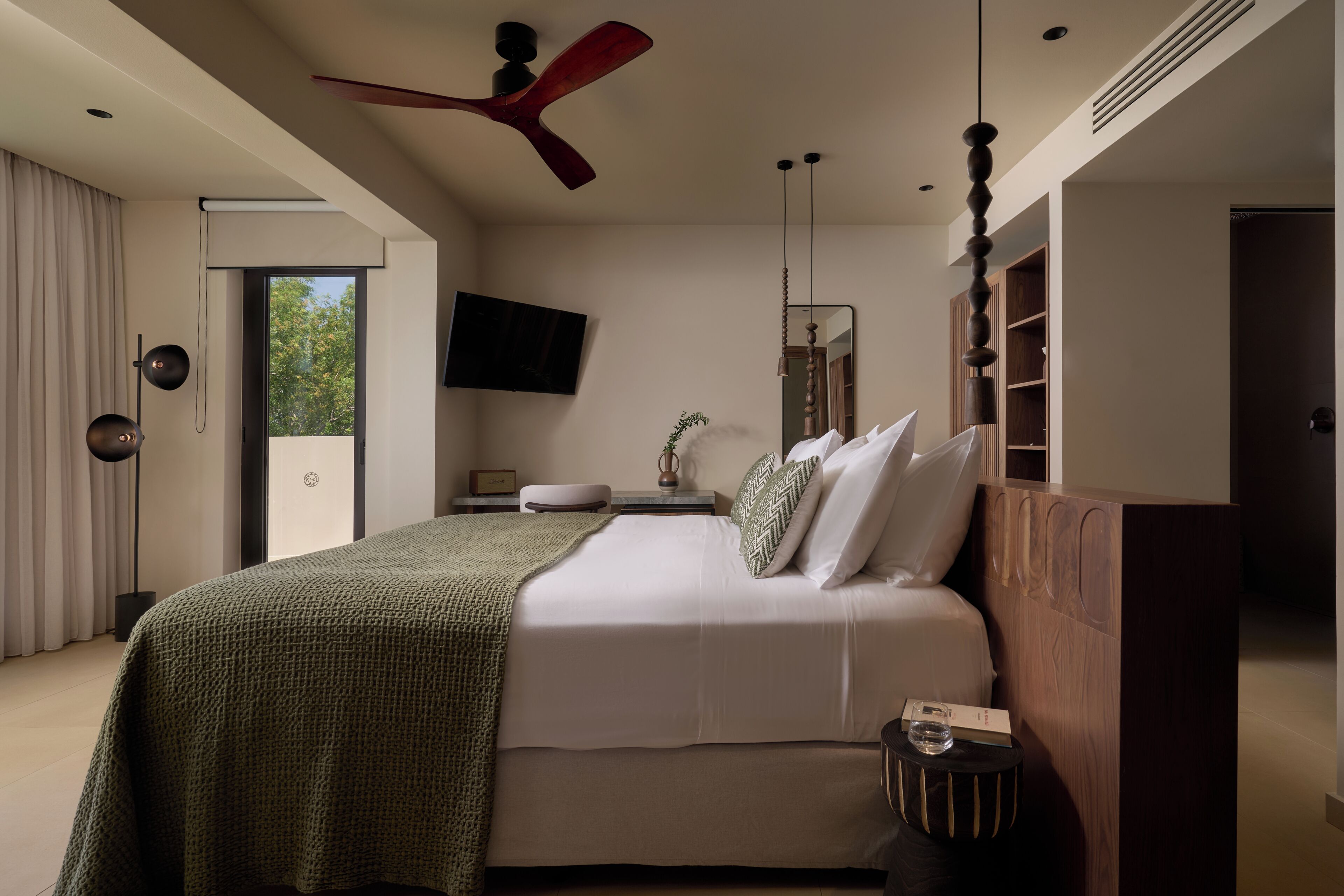 A modern bedroom with a bed, a ceiling fan, a TV, and a view of the outdoors.