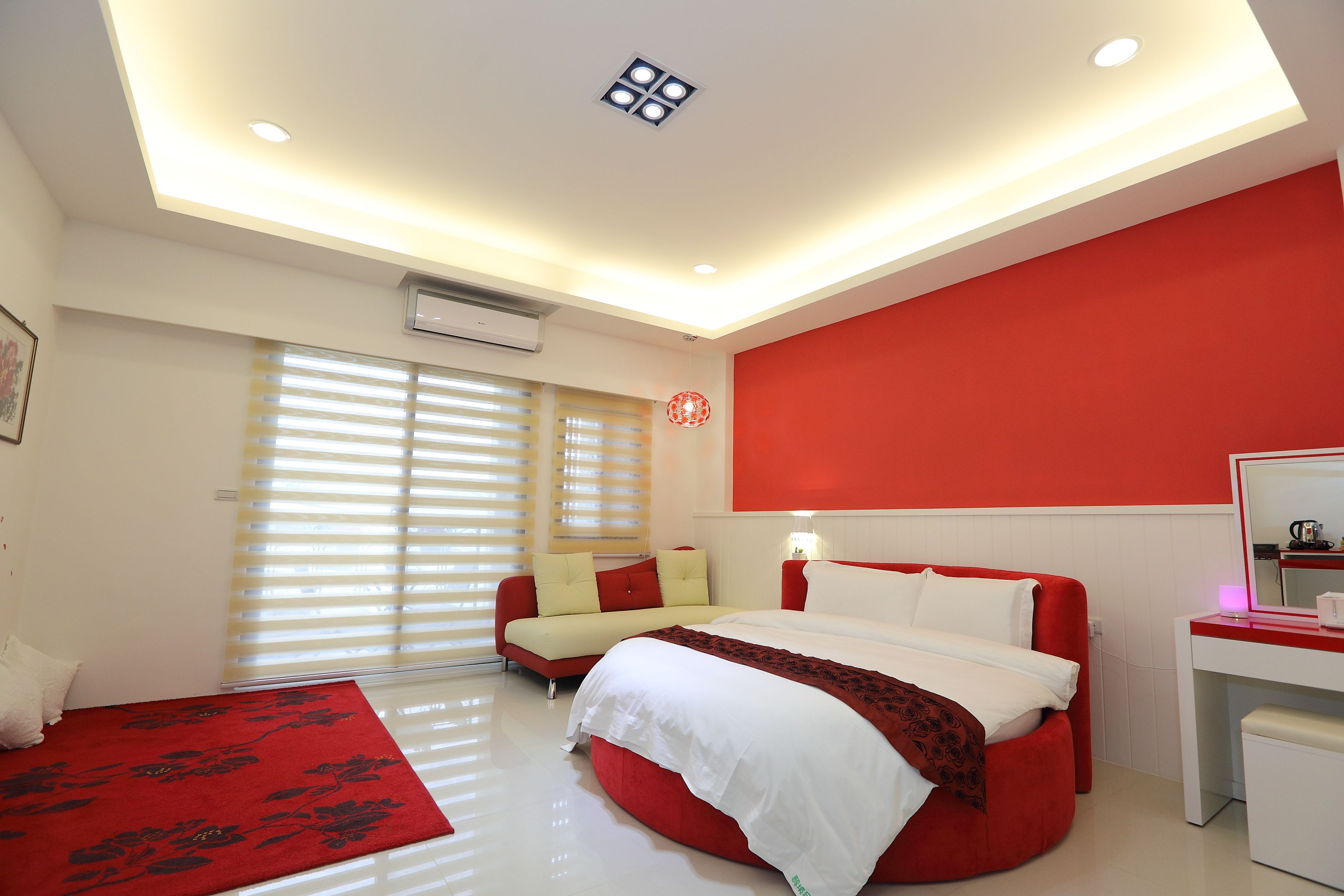 A modern bedroom with a red and white color scheme, a bed, a desk, and a sofa.